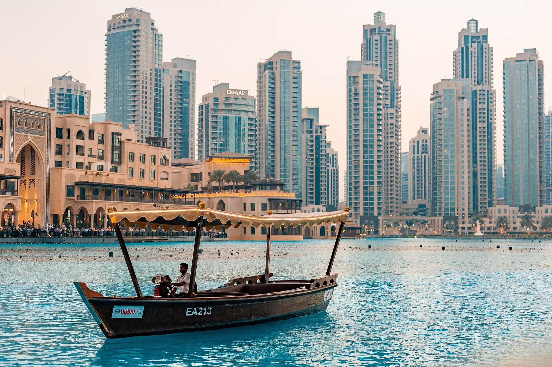 A traditional abra boat sailing on the lake with skyscraper luxury hotels and EMAAR towers in the background near the Dubai Mall showcasing the best hotels in Dubai near Dubai Mall